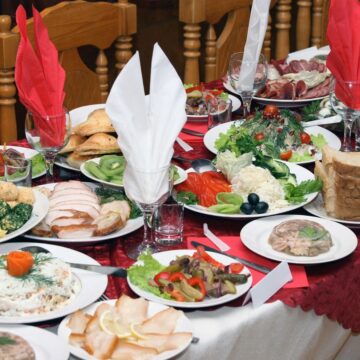 The table is filled with various dishes, including meats, salads, breads, and garnished plates—a perfect setting for a healthier holiday feast. Red and white napkins are neatly folded on the red-and-white tablecloth, with wooden chairs inviting guests to enjoy simple tips for guilt-free indulgence.