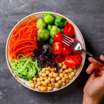 An image of a hand holding a fork over a plate of different vegetables.