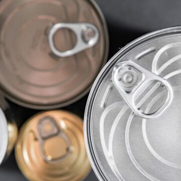 Close-up view of various unopened metal cans with pull tabs, embodying the convenience of canned foods for anytime meals. The cans, in differing colors such as silver and gold, are scattered across a dark surface.