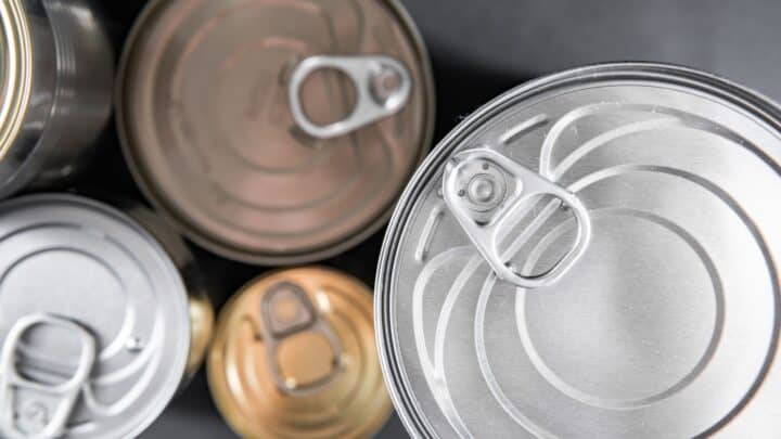Close-up view of various unopened metal cans with pull tabs, embodying the convenience of canned foods for anytime meals. The cans, in differing colors such as silver and gold, are scattered across a dark surface.