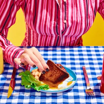 Three people are seated at a table with plates of fried chicken, corn on the cob, and classic '90s drinks. The sun is shining brightly, casting a warm glow and drawing attention to the nostalgic vibe of the meal rather than the individuals present.