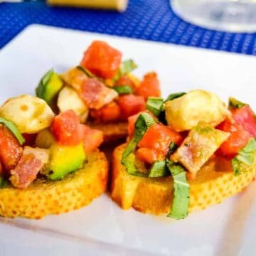 Loaded bruschetta salad on crostini on a white plate.