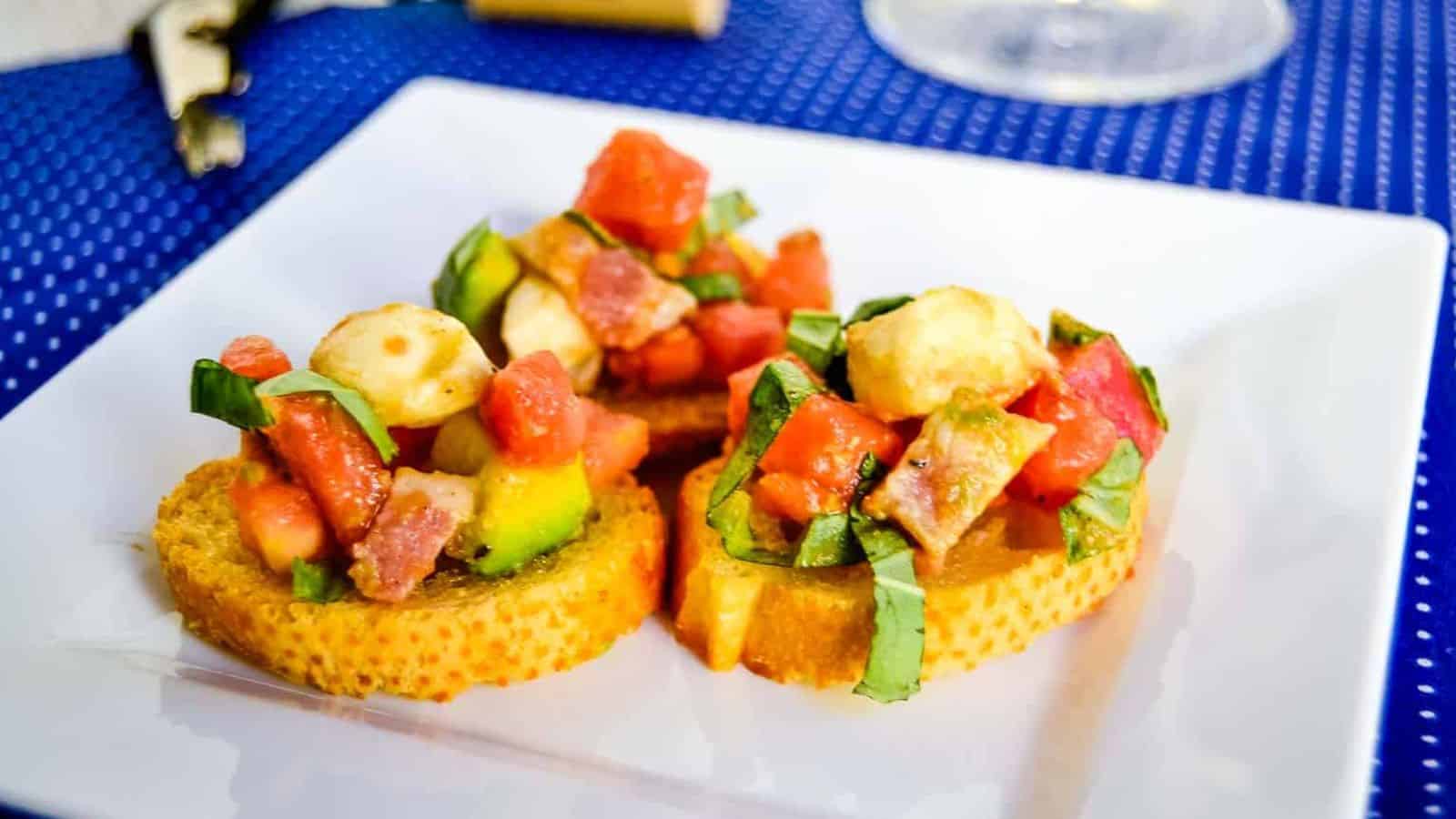 Loaded bruschetta salad on crostini on a white plate.