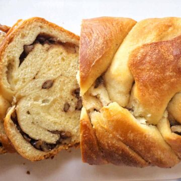 A sliced loaf of braided bread with a cinnamon and nut filling rests invitingly on a white surface, showcasing its delightful layers. This is truly one of the good breads, offering a comforting treat that can be enjoyed any time of day.