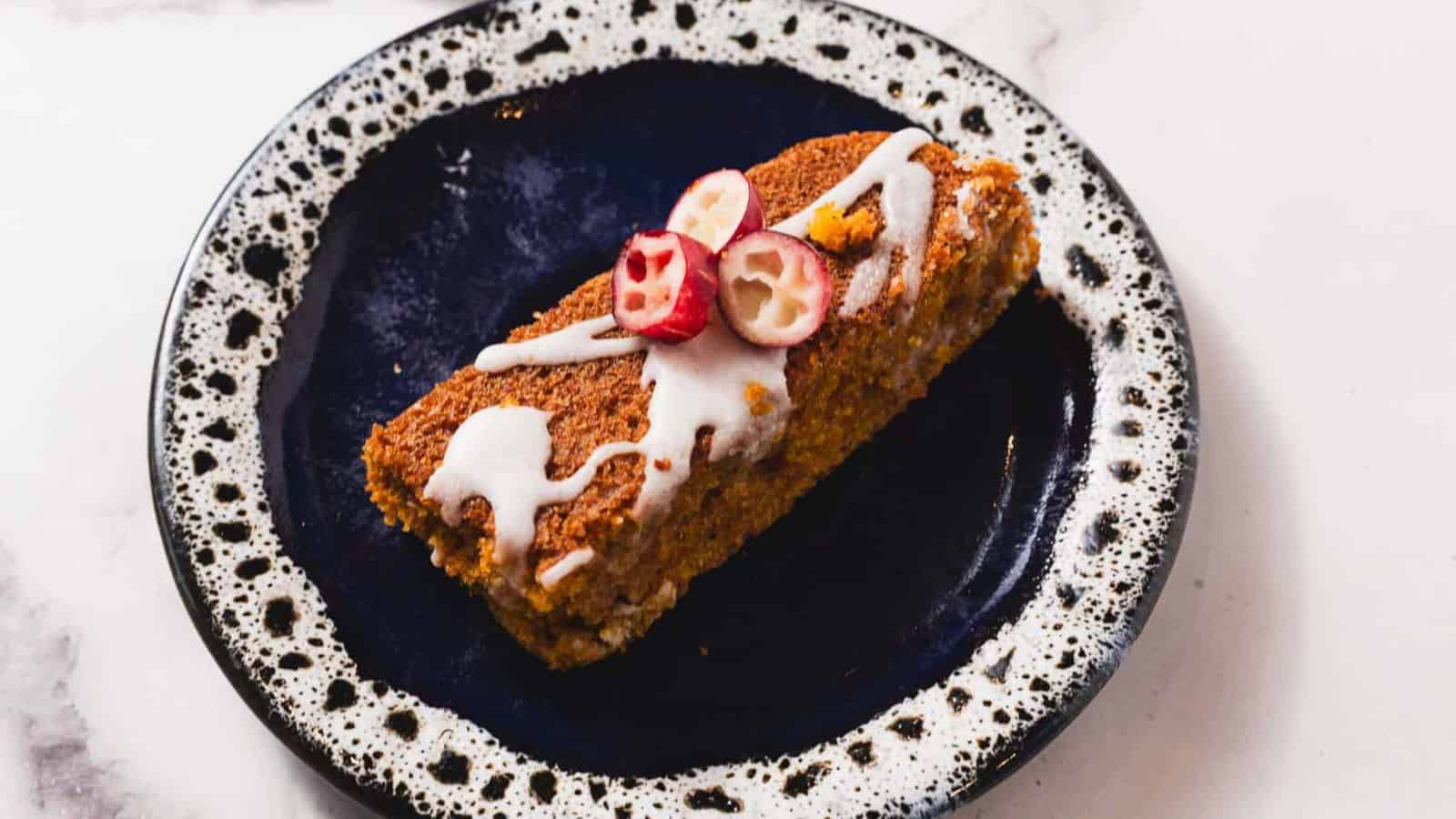 Sliced pumpkin bread topped with white icing and small cranberry slices, arranged on a wooden cutting board. The bread appears moist with a sprinkling of spices on top.