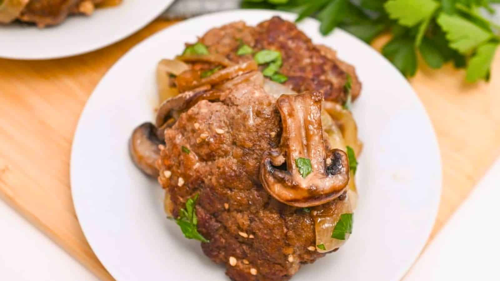 White plate with salisbury steak on it and a mushroom on top of them.