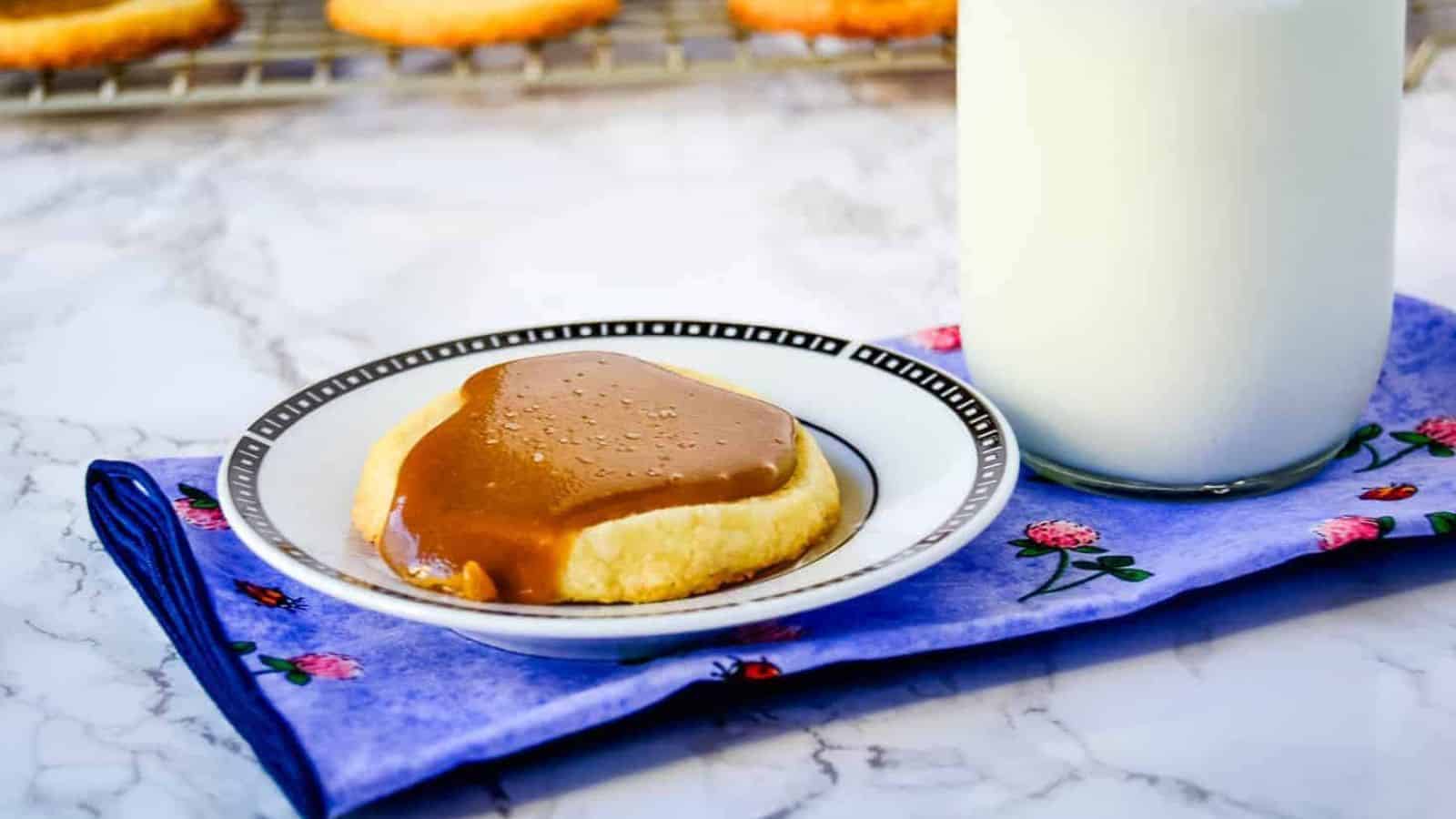 One Salted Bourbon Caramel Shortbread Cookies cookie on a white plate next to a bottle of milk.