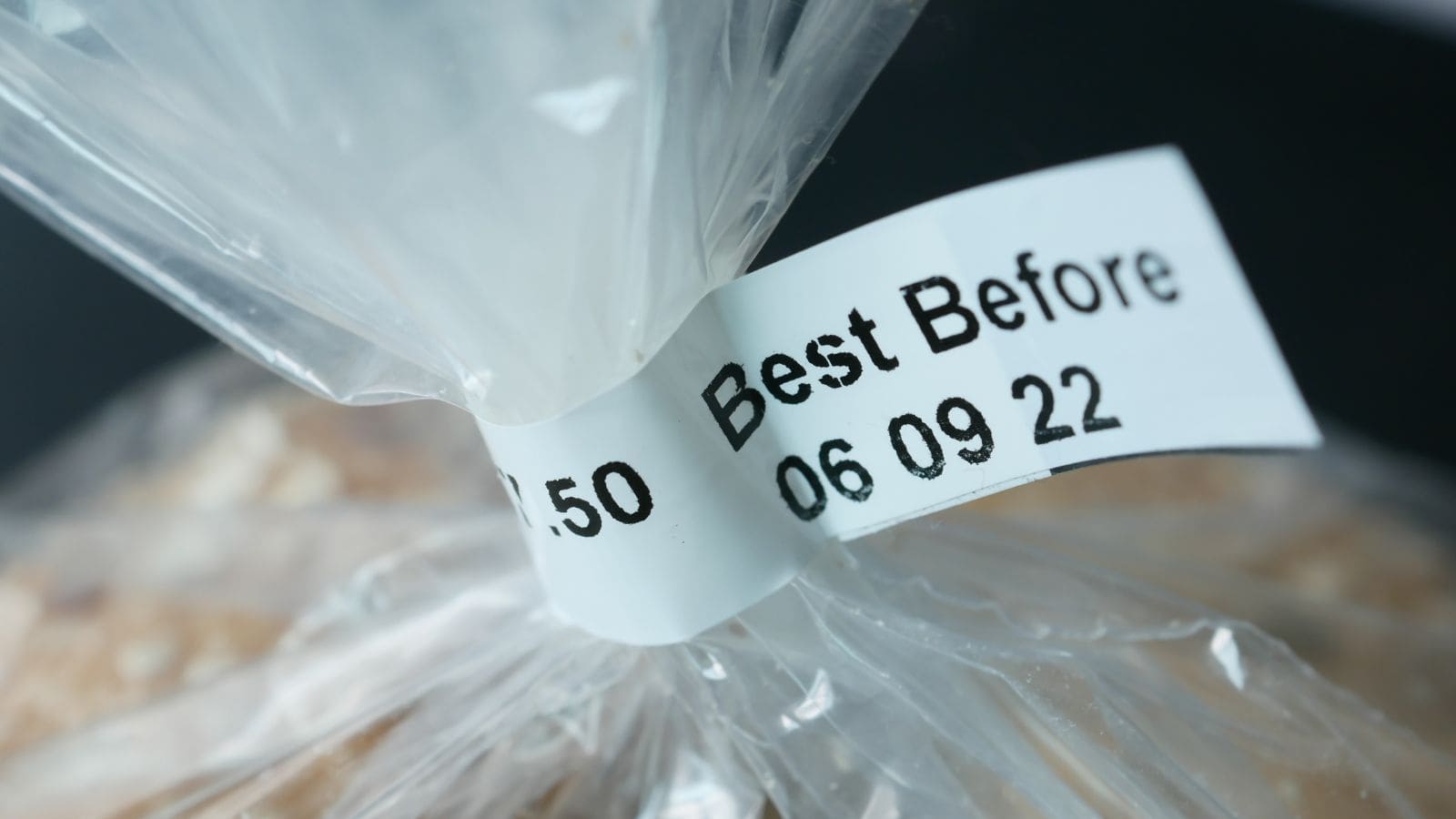A close-up of a plastic bag tied at the top with a white label attached hints at holiday meal planning tips. The label displays the text "Best Before 06 09 22" and another partly visible number "£.50" against a slightly blurred background.