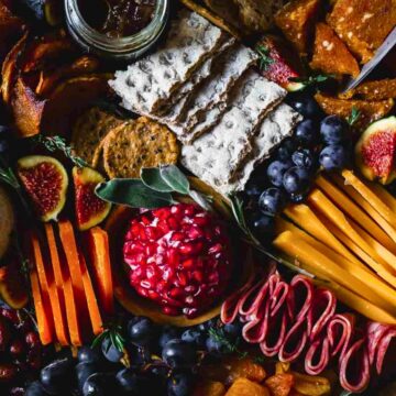 A charcuterie board featuring assorted cheeses, sliced meats, figs, grapes, dried fruits, nuts, vegetables, and crackers.