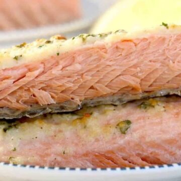 Two pieces of cooked salmon are stacked on a blue and white plate, perfect for easy meals. The salmon appears flaky with some herbs and a lightly browned crust on top. In the background, a slice of lemon and green garnish add just the right touch for simple dinner ideas.