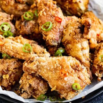 A plate of crispy, crowd-pleasing fried chicken wings garnished with sliced green chilies. The wings are arranged on a bed of white parchment paper, highlighting their golden-brown coating—a perfect addition to family gatherings.