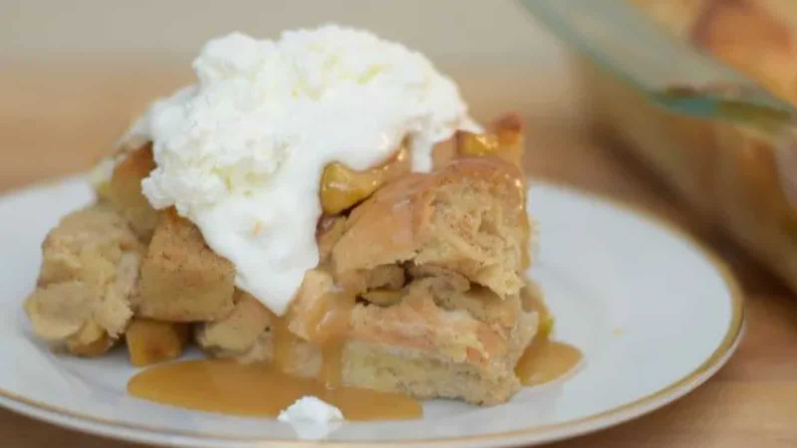 Image shows a head on close up shot of a slice of Apple Pie Bread Pudding topped with whipped cream.