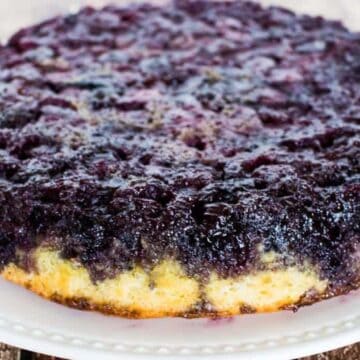 Blueberry upside down cake on a white plate before slicing.