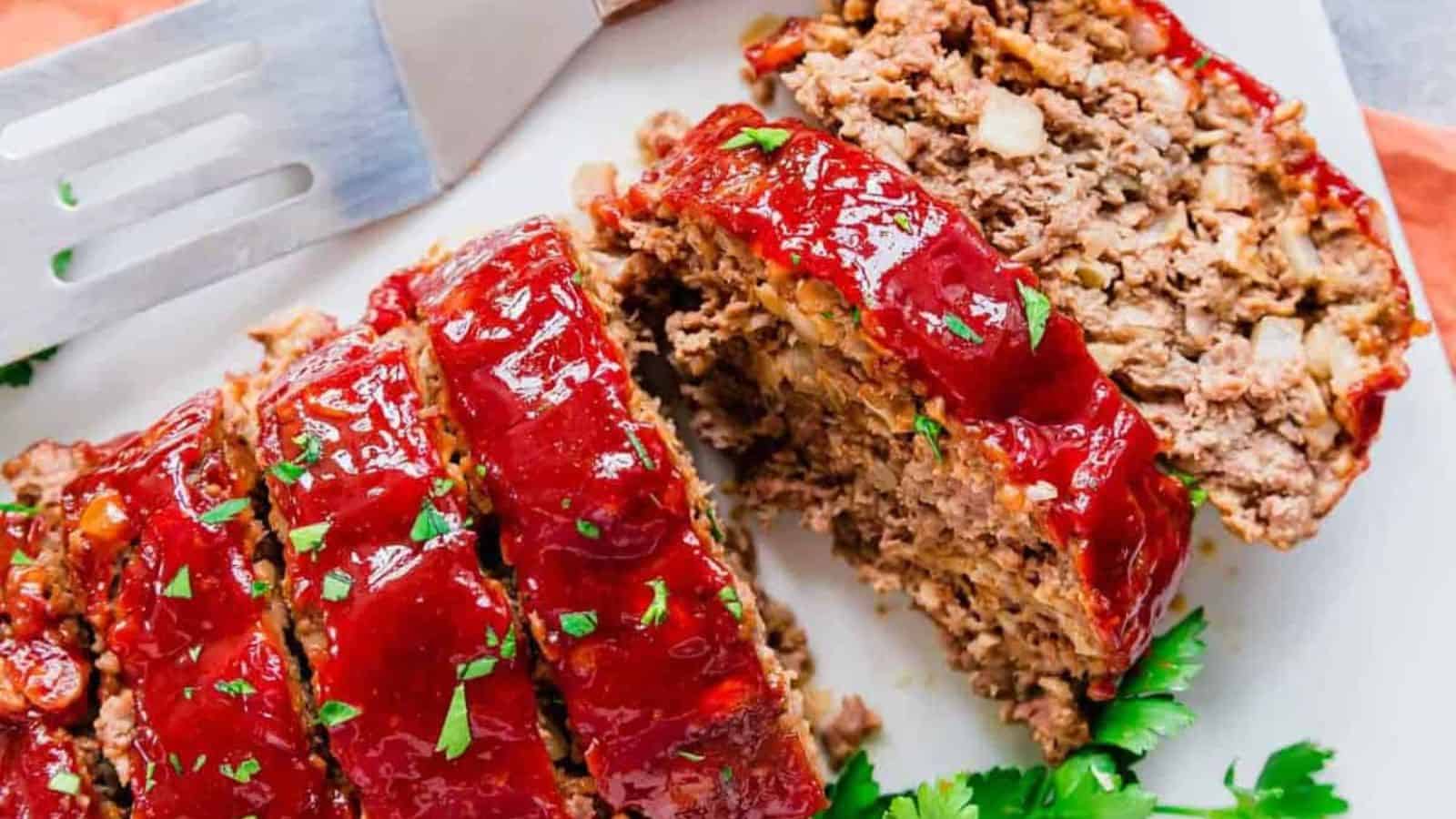 Meatloaf on a white plate cut into slices with fresh parsley garnish.