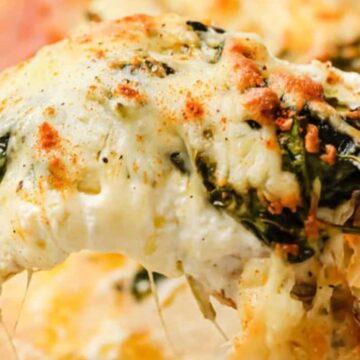 A slice of pizza is being lifted from the whole, topped with melted cheese and spinach. The crust, perfect for when you want to treat yourself, boasts a light dusting of seasoning, while cheese stretches from the slice. The focus is on the toppings and texture of this indulgent delight.