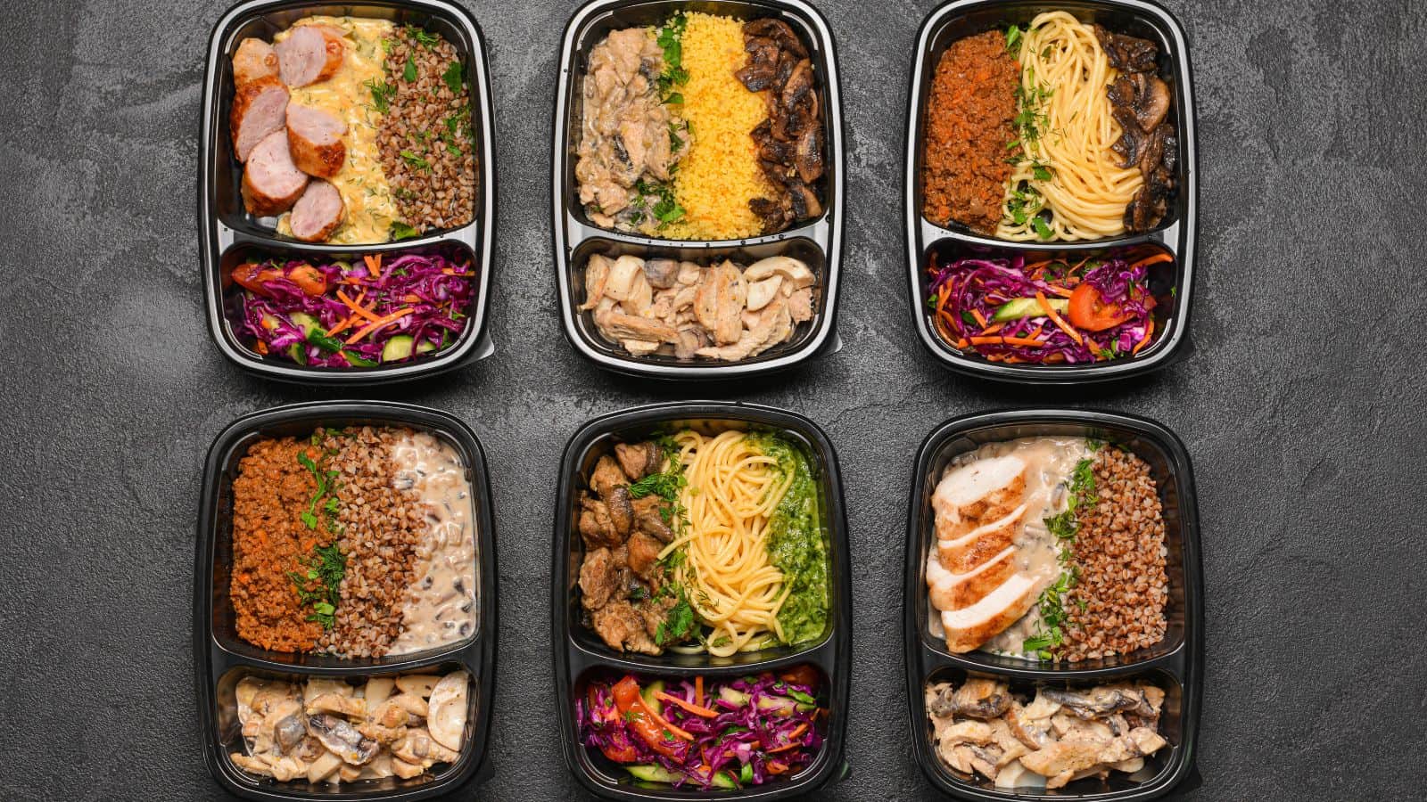 Six meal prep containers on a dark surface, each boasting unique combinations of grains, vegetables, and protein. Dishes include pasta with sliced meats and buckwheat paired with sautéed mushrooms, and colorful salads, showcasing fresh ingredients without any hidden processed foods.