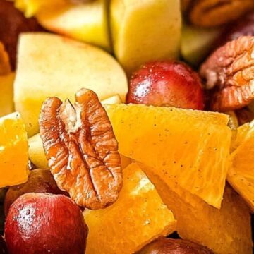 A closeup is shown of Thanksgiving Fruit Salad with apples, grapes, pears, oranges, and pecans.