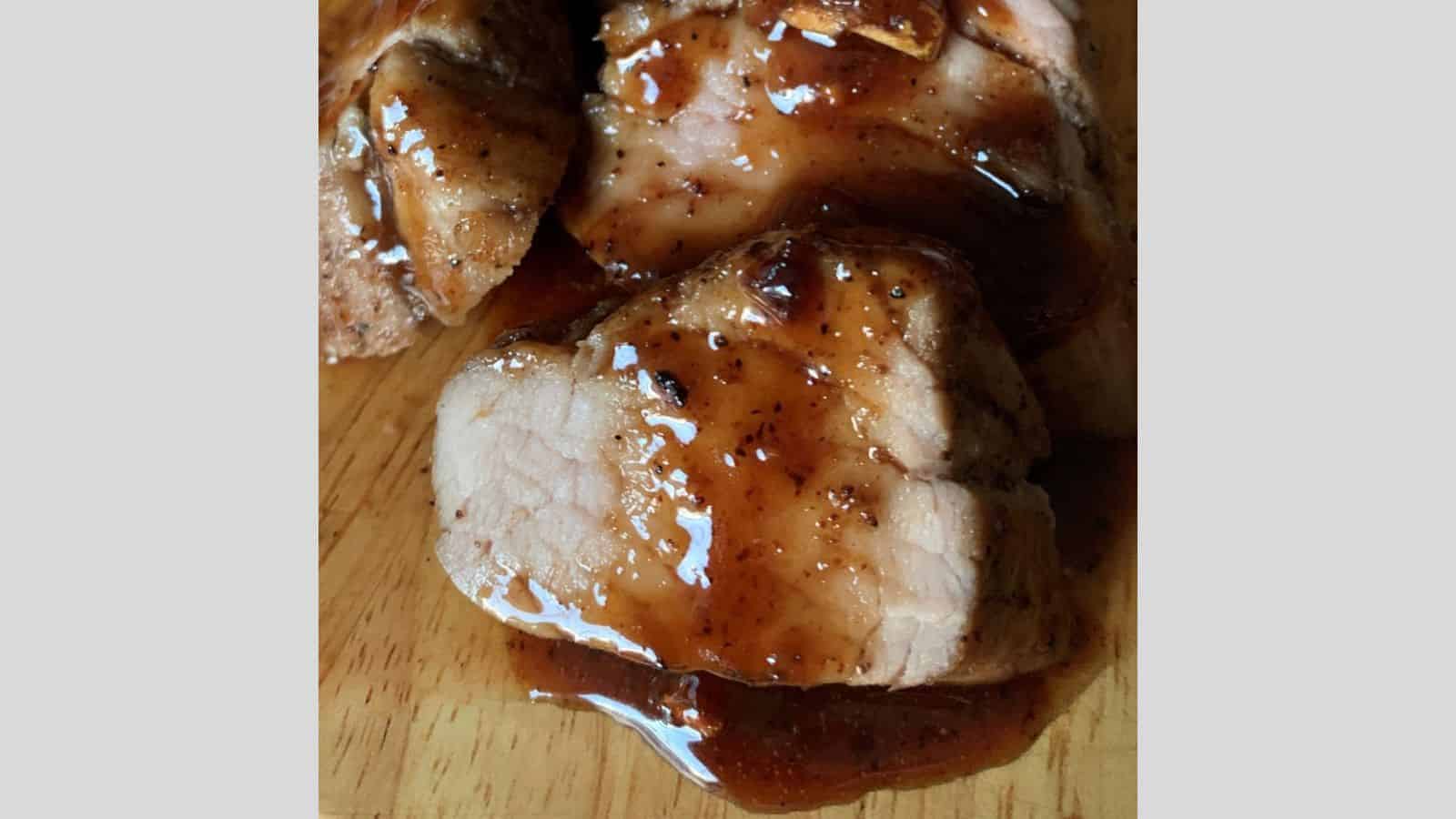 Slices of cooked meat, covered in a glistening brown sauce, present a show-stealing meal, elegantly arranged on a wooden surface.