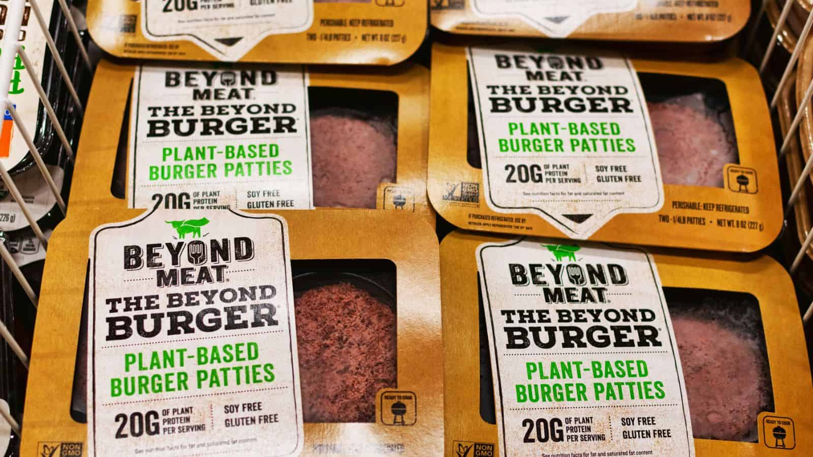 Packages of Beyond Meat plant-based burger patties are displayed in a store. The packaging highlights that the patties are soy-free, gluten-free, and contain 20 grams of protein per serving.
