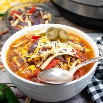 Low angle shot of a white bowl filled with tortilla soup. There is an instant pot in the background.
