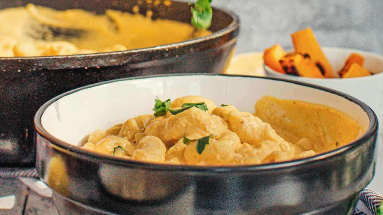 A bowl of creamy pasta garnished with herbs is in the foreground, perfect for even the pickiest eaters. In the background, a black pot with more pasta and a small bowl with roasted vegetables promise good recipes for every family meal.