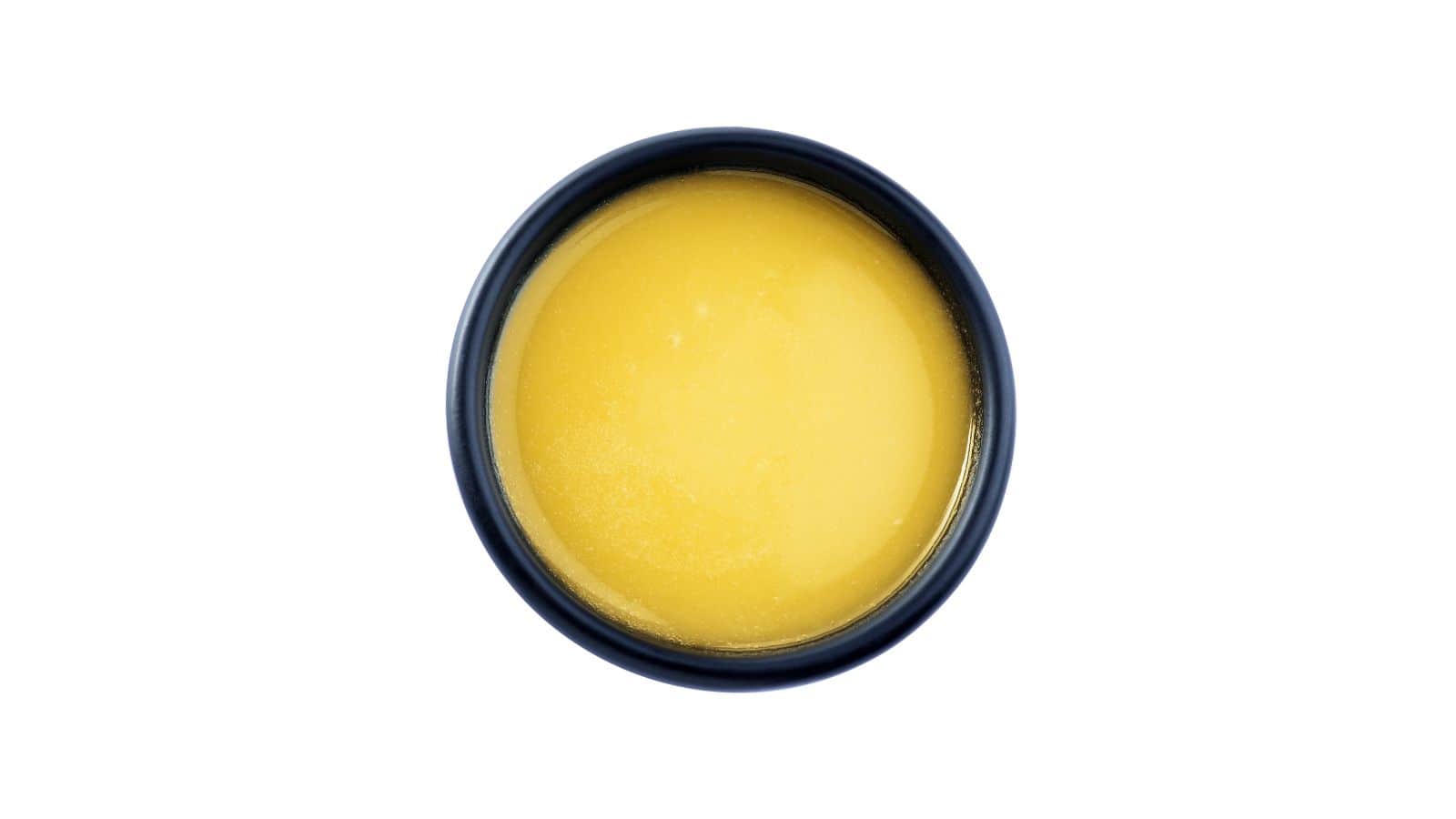 Aerial view of a small black bowl containing a smooth, yellow substance, possibly ghee or melted butter, placed on a white background. This healthy oil option stands in stark contrast to the typical toxic oils found in many kitchens.