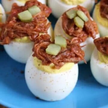 Deviled eggs topped with shredded meat and diced pickles are arranged on a blue plate.