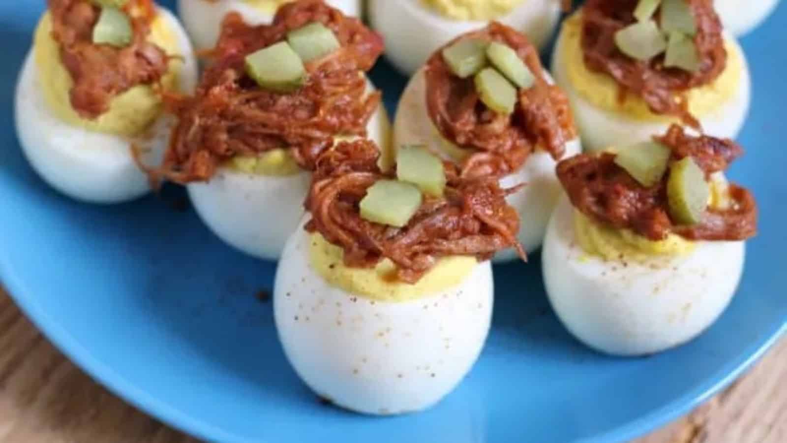 Blue plate with pulled pork deviled eggs, all topped with a pickle.