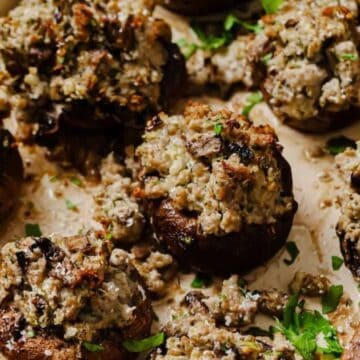 A baking tray filled with festive appetizers, these stuffed mushrooms are topped with a mixture of herbs, cheese, and breadcrumbs, garnished with chopped parsley. Perfect as holiday snacks or party food, the golden brown stuffing is irresistibly crispy.