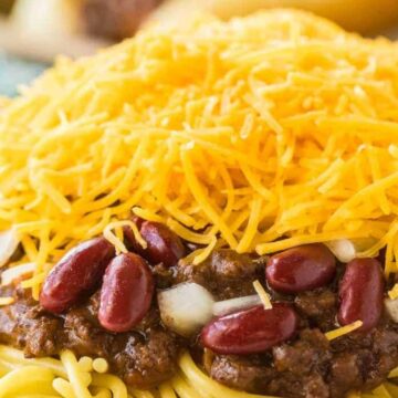 A plate of spaghetti topped with chili, red kidney beans, chopped onions, and a generous layer of shredded cheddar cheese.