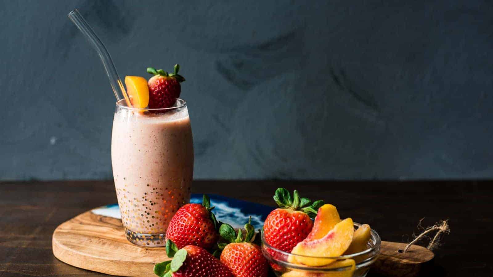 A strawberry peach smoothie on a wood board next to strawberries and peaches with text overlay for social media.