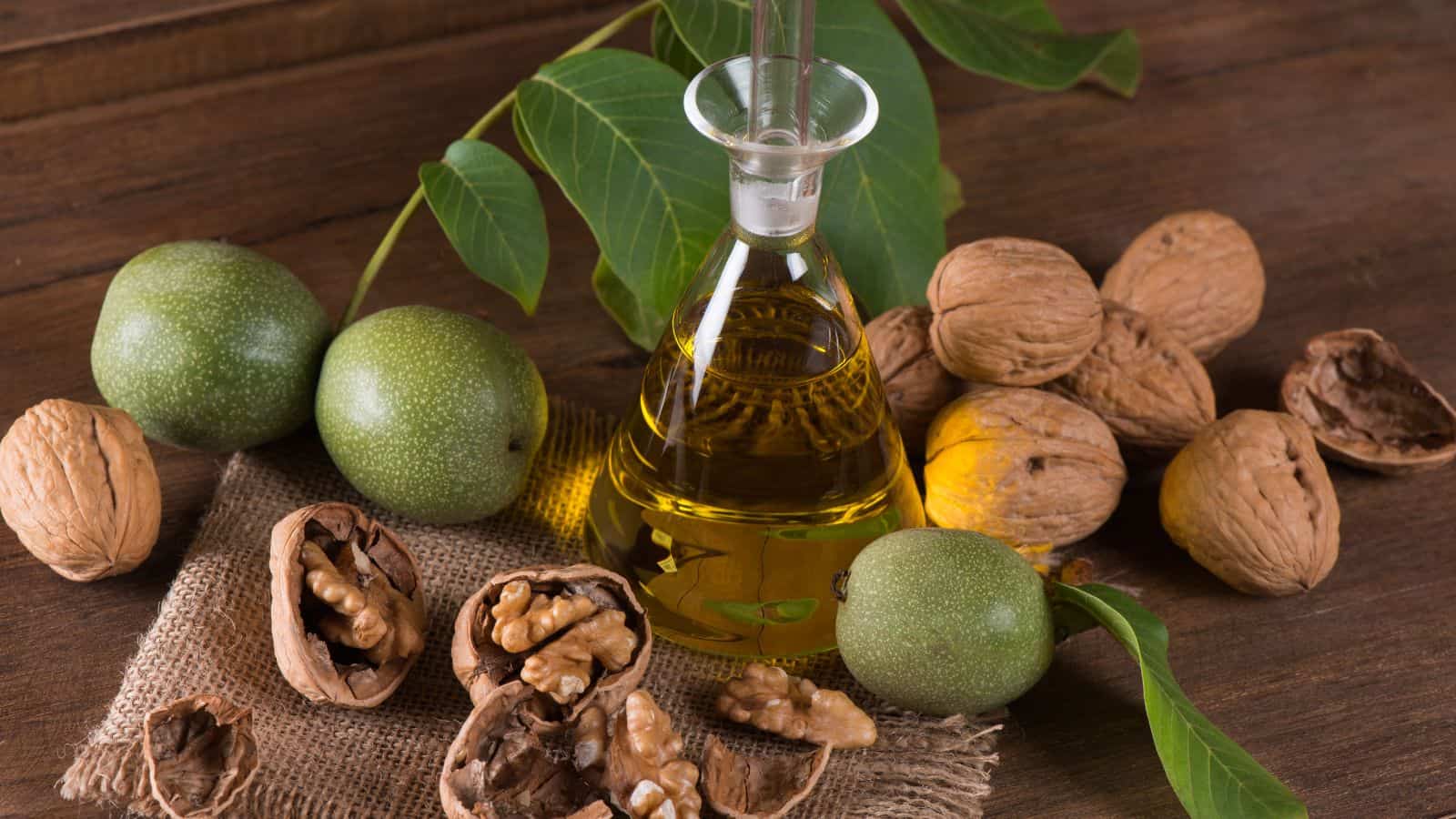 A glass bottle of healthy walnut oil sits on a wooden surface, surrounded by whole and cracked walnuts, some green and some in shells. Fresh leaves add a natural element to the arrangement, highlighting the contrast between toxic oils and this nourishing choice.