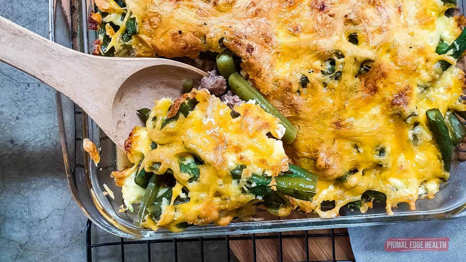 Green bean casserole being served with wooden spoon.