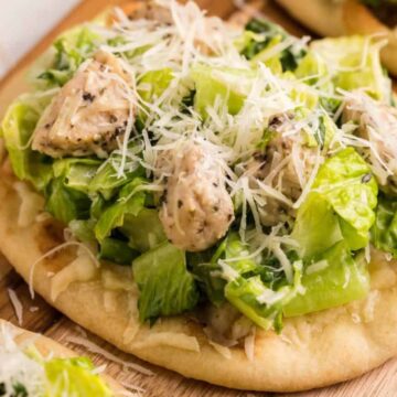 A delightful dinner option, this flatbread features seasoned chicken pieces with chopped romaine lettuce and a generous sprinkle of shredded parmesan cheese. Perfect for serving guests, it's elegantly presented on a wooden board, making it an ideal snack to savor.