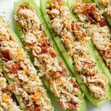 Cucumber slices are topped with a shredded chicken mixture, including pieces of bacon and herbs, arranged neatly on a plate.