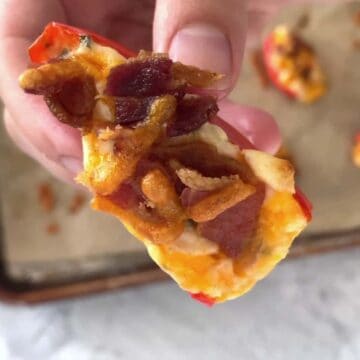 A hand holding a mini pepper topped with bacon.