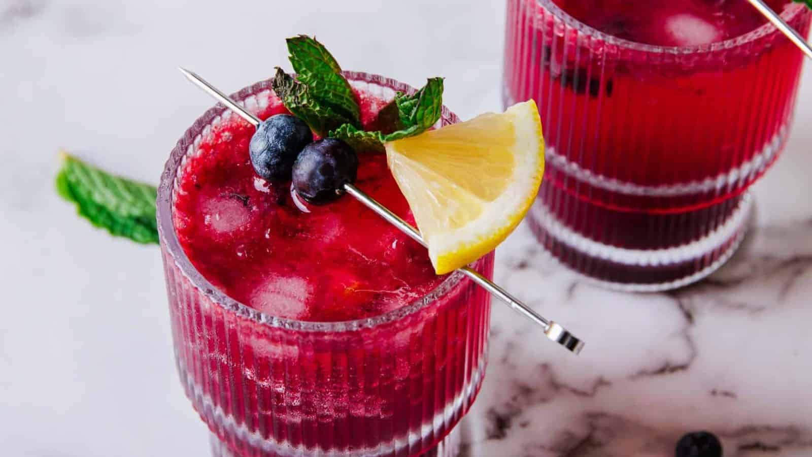 A close-up of a blueberry mojito mocktail garnished with fresh mint, blueberries, and a lemon wedge.