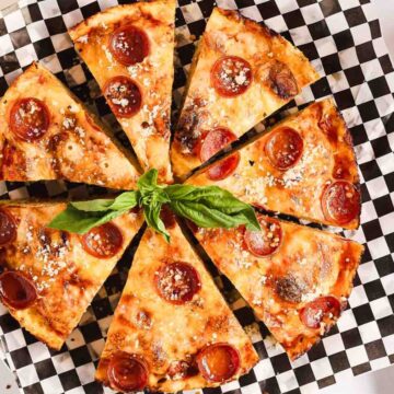 Sliced pepperoni pizza on a checkered platter garnished with fresh basil.