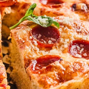 Close-up of cheesy pepperoni pizza with a garnish of fresh basil.