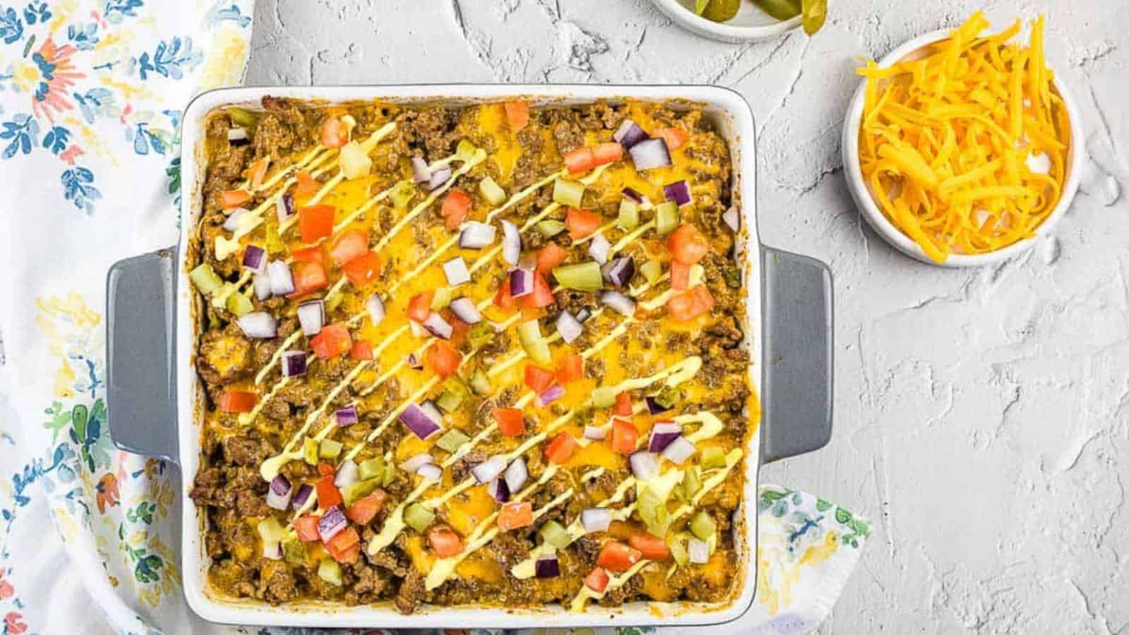 A top-down shot of Cheeseburger Casserole with pickles and cheese nearby.