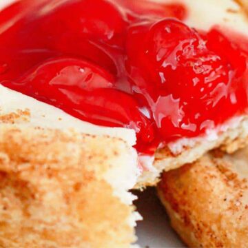 Close-up of a pastry with a crumbly crust, perfect for brunch, filled with creamy cheese and topped with bright red cherry filling to impress your guests.