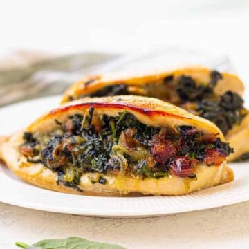 A special low-carb dish, this white plate features two pieces of stuffed chicken breast, filled with spinach and sun-dried tomatoes. Fresh spinach leaves are artfully scattered on the table surface, adding a touch of elegance perfect for Valentine’s Day.