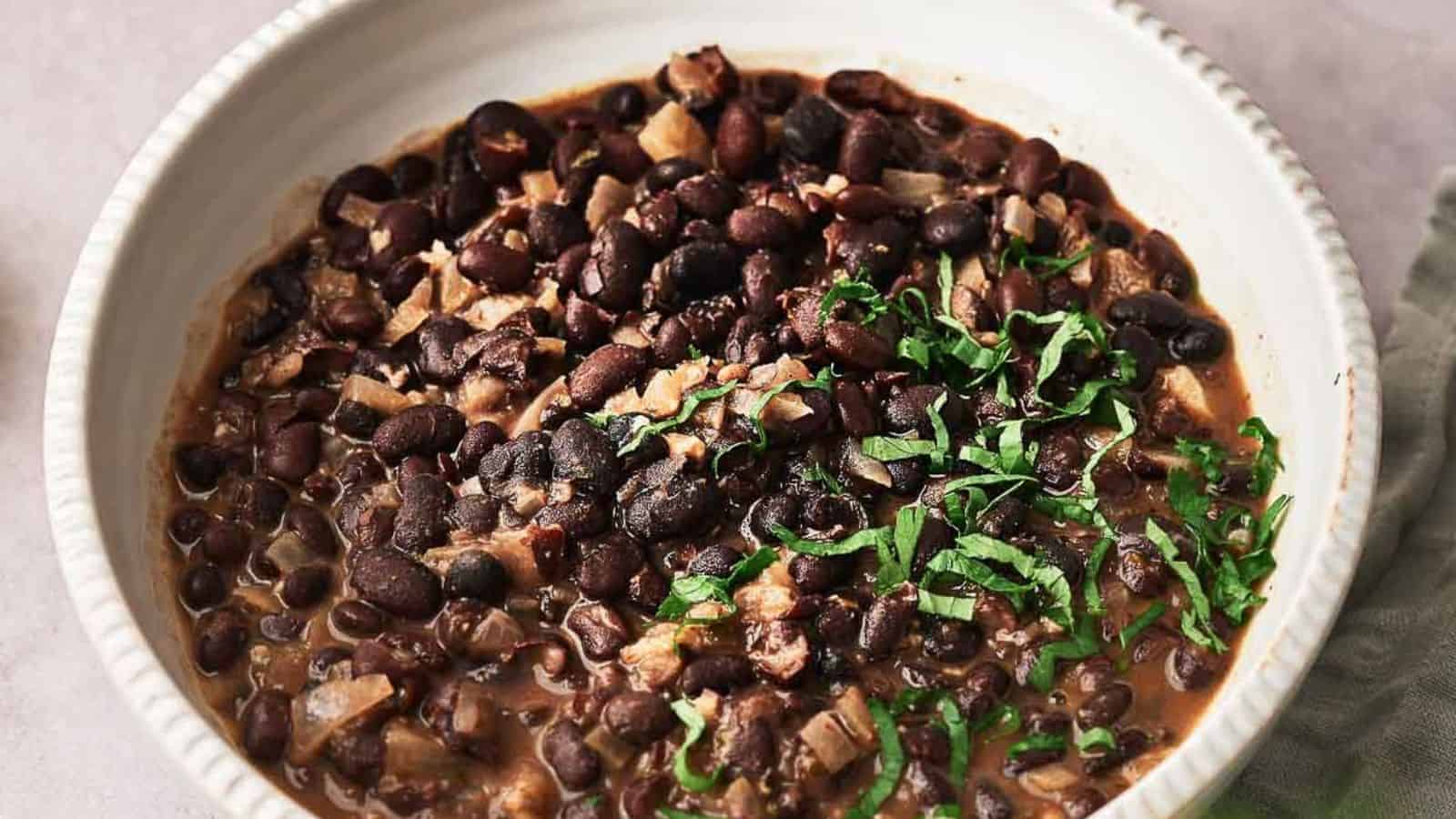 A white bowl filled with cooked black beans mixed with chopped onions and garnished with fresh herbs.