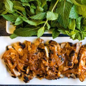 Gochujang chicken on a platter with fresh herbs.