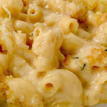 Close-up view of a serving of macaroni and cheese. The dish features creamy cheese sauce and is topped with a layer of golden-brown breadcrumbs. The macaroni is well-coated and on a white plate.