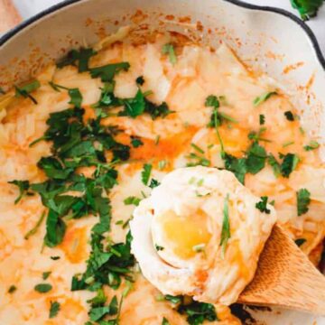 A pot of mouthwatering cheesy mashed potatoes topped with chopped herbs sits invitingly, with a wooden spoon resting within. Fresh herbs and tomatoes add a splash of color to the marble countertop. Ready in under 1 hour, this dish is perfect for entrees that leave everyone craving more.
