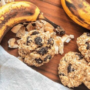 A wooden surface showcases a ripe banana next to several oatmeal raisin cookies, which disappear in minutes. Shredded coconut flakes are scattered around, and a linen cloth partially covers the bottom left corner of the image—an irresistible scene straight from top cookie recipes.