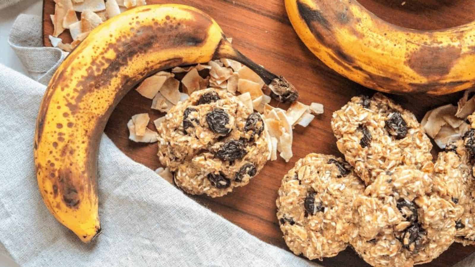 A wooden surface showcases a ripe banana next to several oatmeal raisin cookies, which disappear in minutes. Shredded coconut flakes are scattered around, and a linen cloth partially covers the bottom left corner of the image—an irresistible scene straight from top cookie recipes.