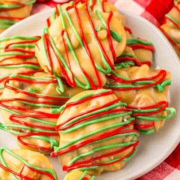 A plate of holiday-themed cookies is placed on a red and white checkered cloth. The cookies are drizzled with red and green icing over a caramel-colored base, surrounded by red and white candy beads.