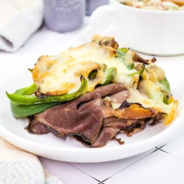 A white plate with a Philly Cheesesteak Stack and a bowl of soup.